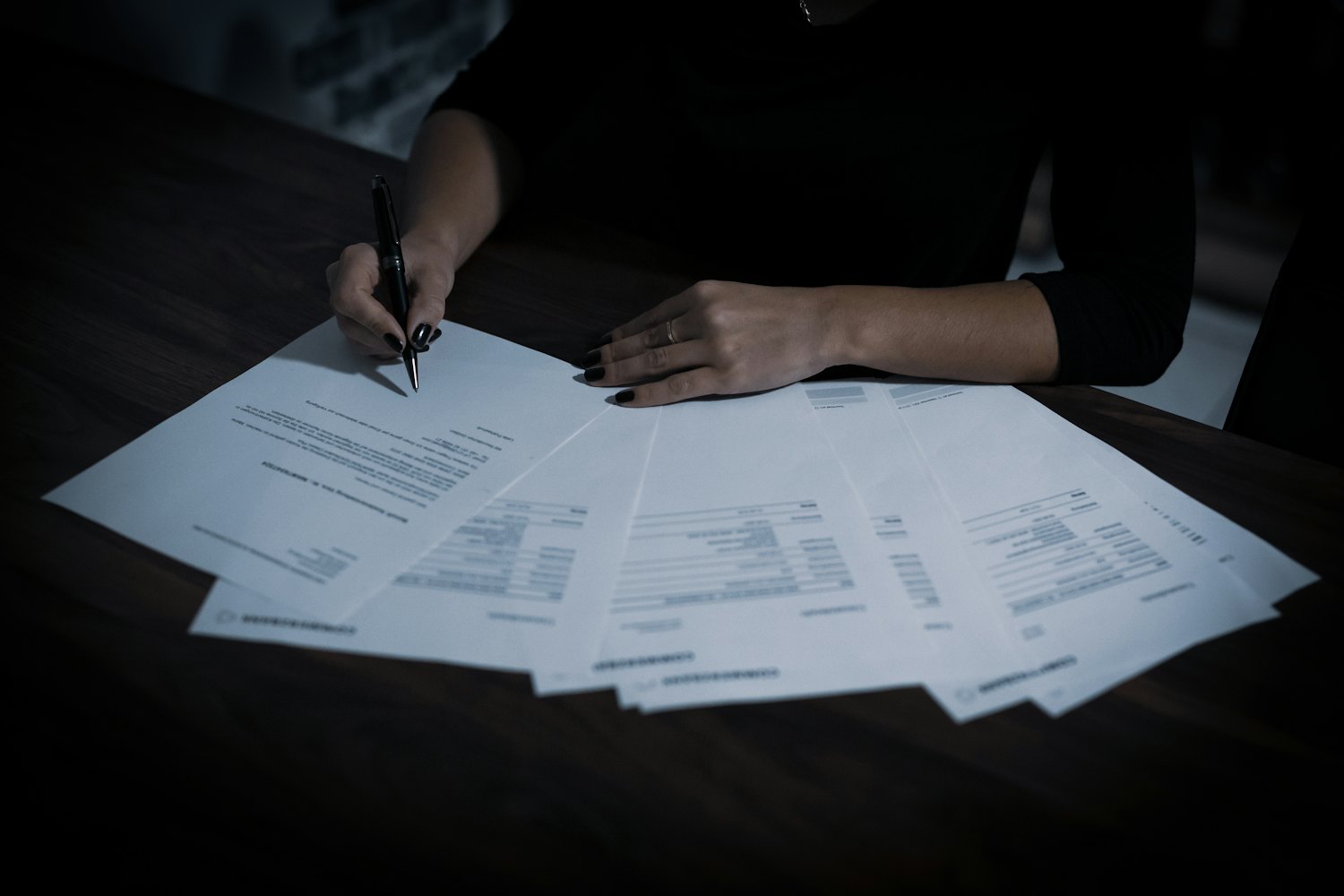 A finance worker signing off a set of printed statements laid out side by side across a desk.