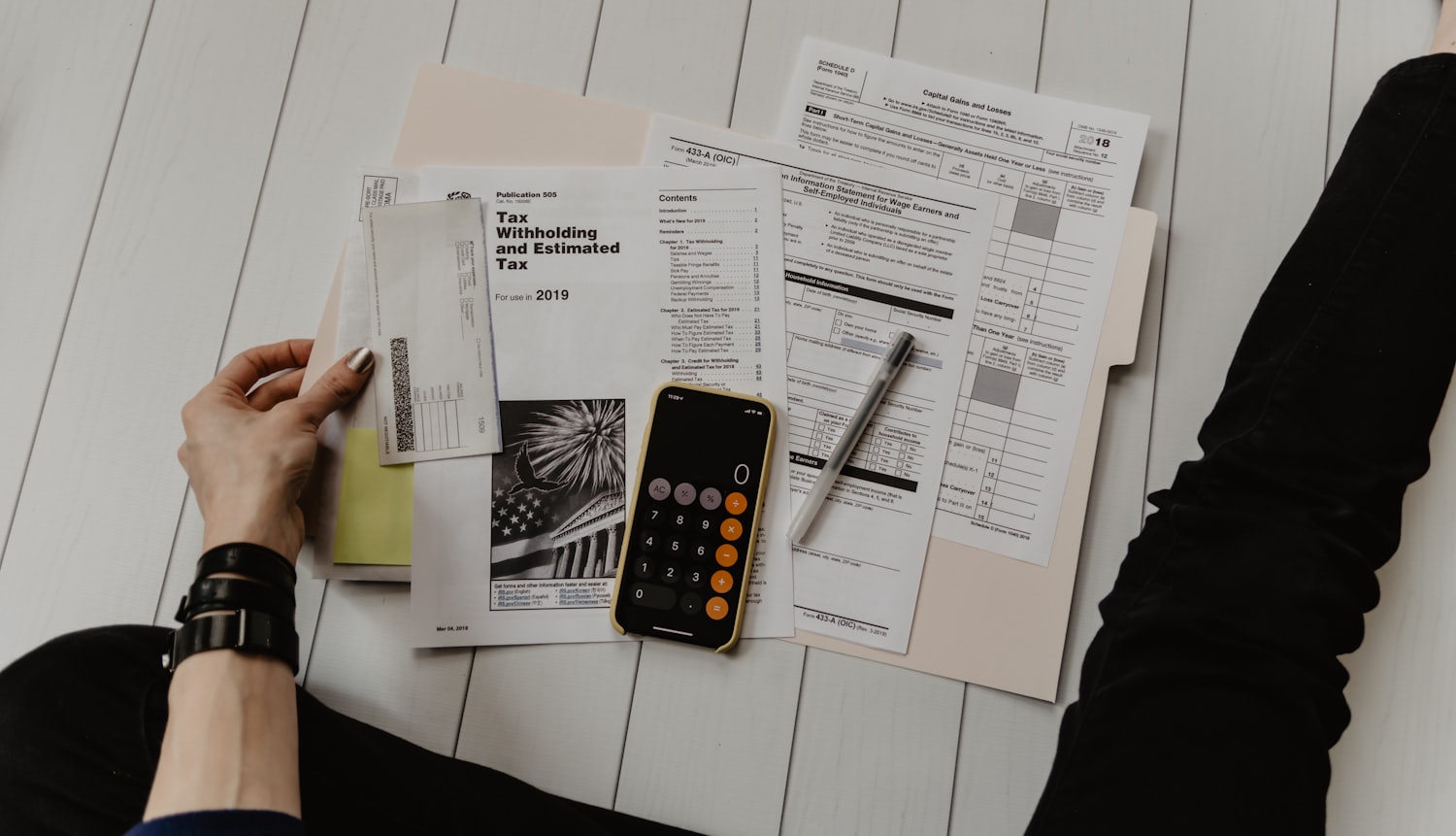 A small run of printed paperwork spread out and worked through by hand, with a pen and a phone calculator.