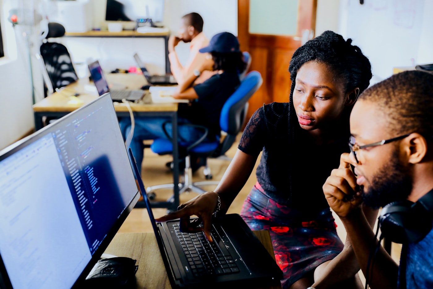 Two engineers reviewing code together on a laptop at a shared desk in an open office